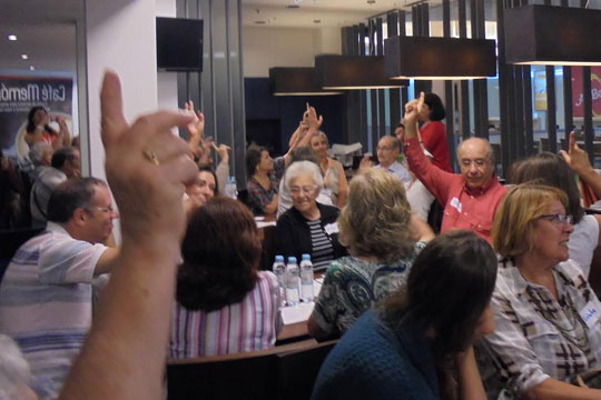Participantes do Café Memória, com a mão levantada.