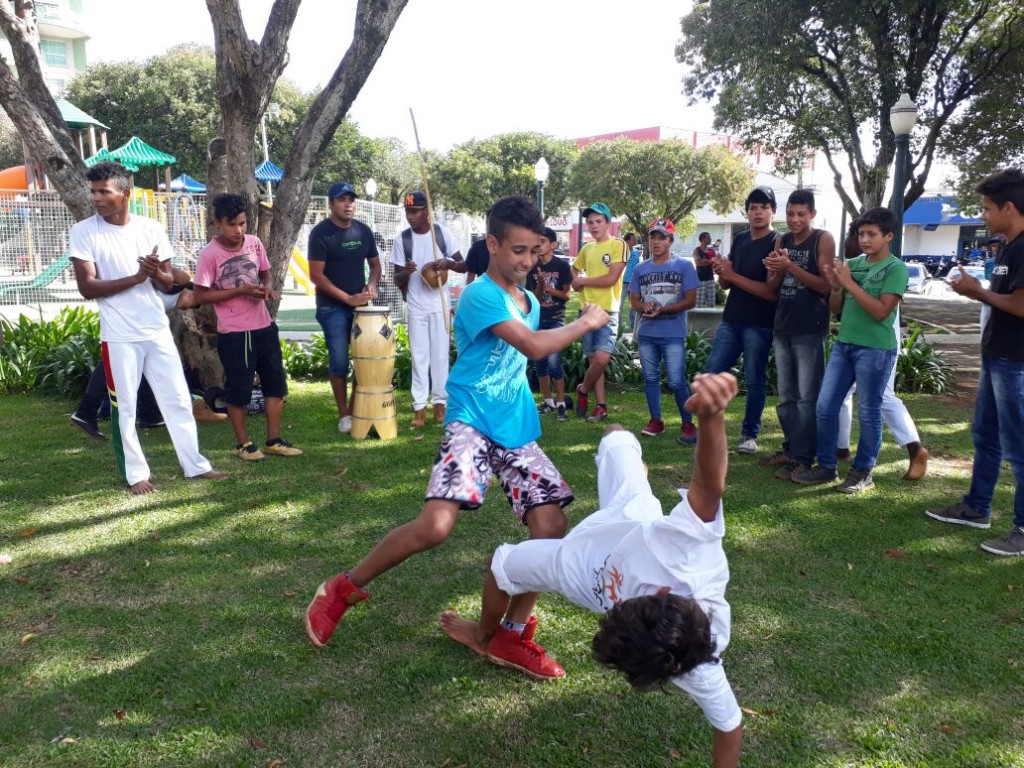 Alunos jogam capoeira em praça próxima à escola